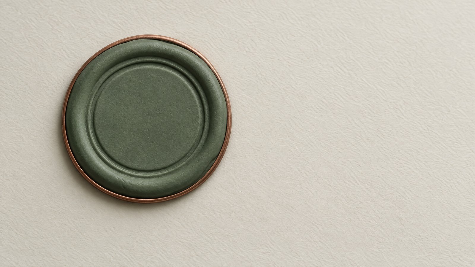 A round sage green clay seal with a thin copper rim pressed onto an off-white surface