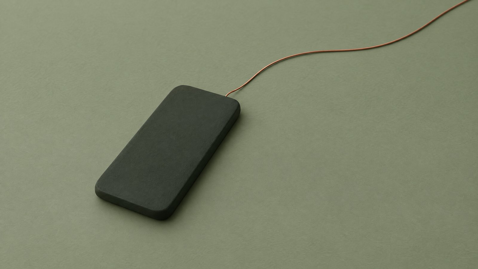 A blank dark green phone-shaped slab on a sage surface with one copper thread leading away